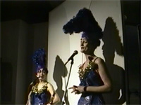 Oliv wearing headdress, speaking into microphone, Haruko Okano in headdress looking on