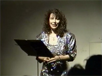 Michael Vonn in an evening gown speaking behind a music stand